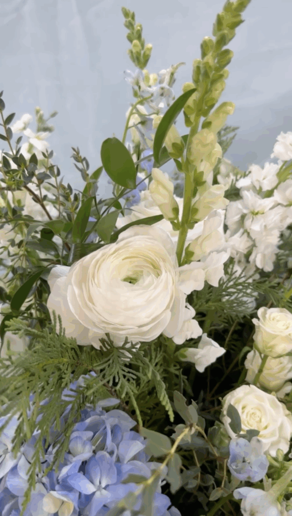 close up of blue hydrangea, ivory ranunculus and greenery.